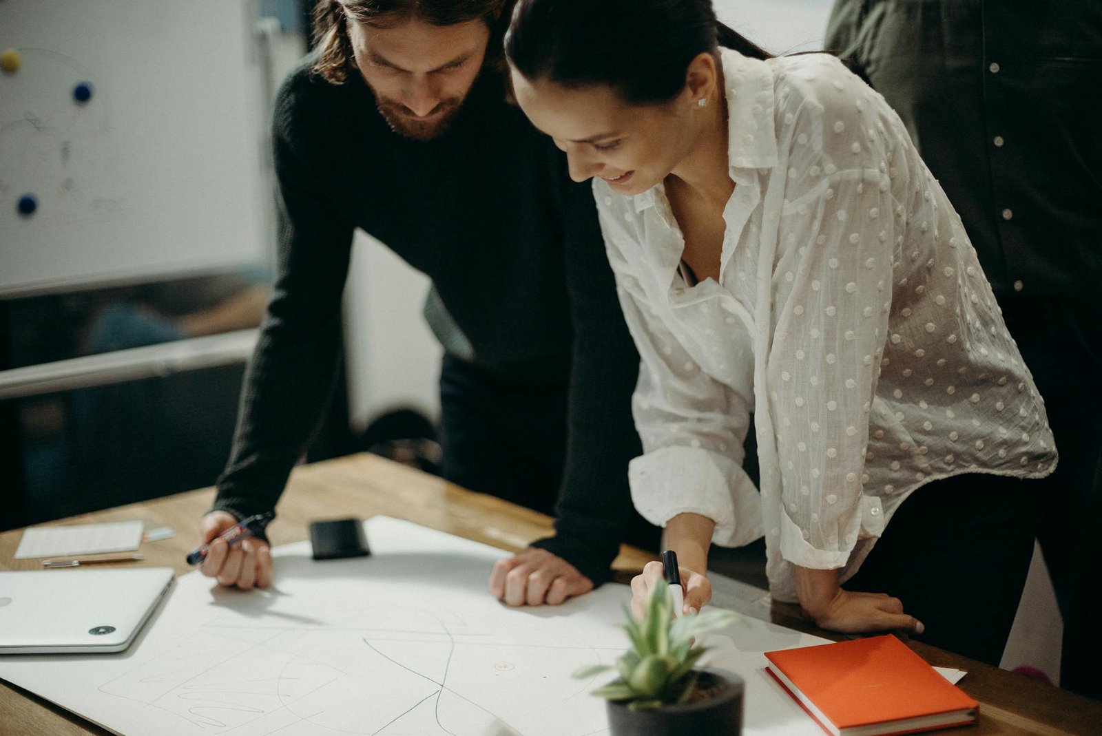 Soft Skills - Behavior - man and woman leaning on table staring at white board on top of table having a meeting man and woman leaning on table staring at white board on top of table having a meeting